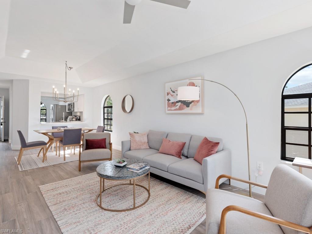 Living room featuring vaulted ceiling, hardwood / wood-style floors, plenty of natural light, and ceiling fan with notable chandelier