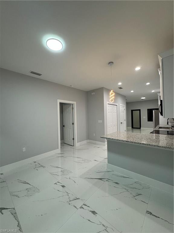 Kitchen with light stone counters, kitchen peninsula, decorative light fixtures, and white cabinetry