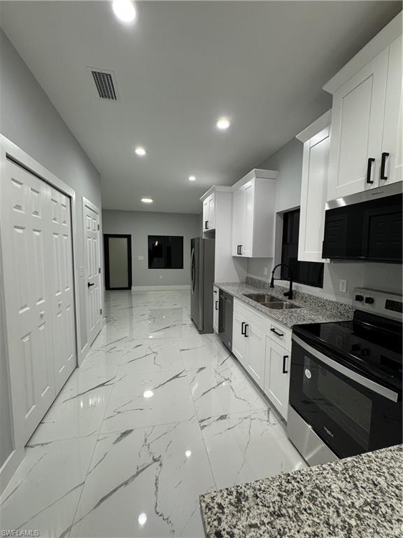 Kitchen with sink, white cabinets, stove, and light stone countertops