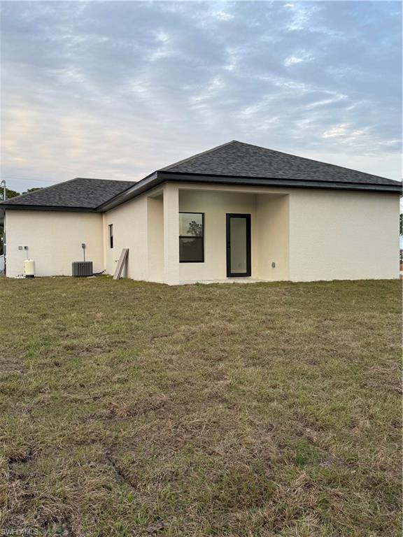 Rear view of property with central AC unit and a lawn
