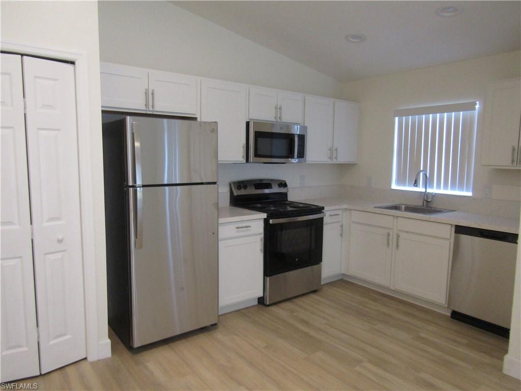 Kitchen featuring stainless steel appliances, white cabinetry, light-toned countertops, wood-finish flooring, and a vaulted ceiling