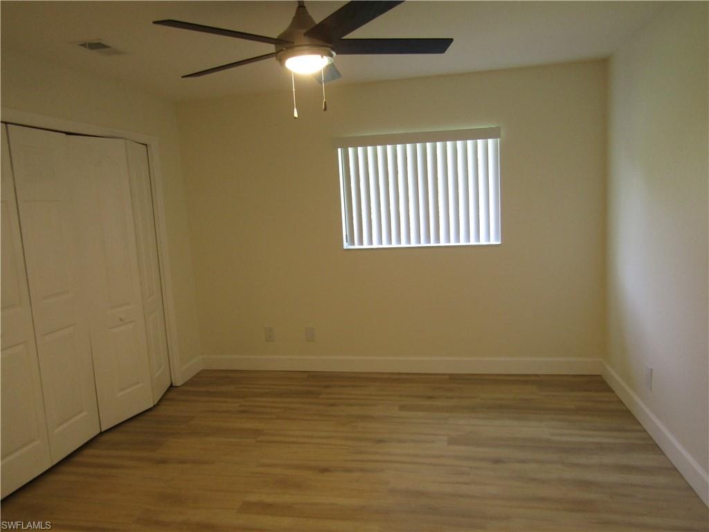 Neutral-toned room featuring wood-finish flooring, a ceiling fan with integrated lighting, a window with horizontal blinds, and bi-fold closet doors