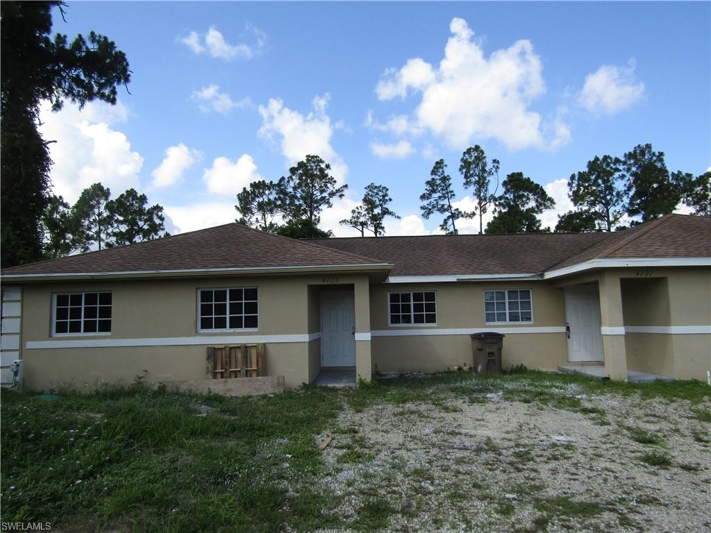 Duplex property featuring a tan stucco exterior, multiple white-framed windows with grilles, and a brown shingle roof