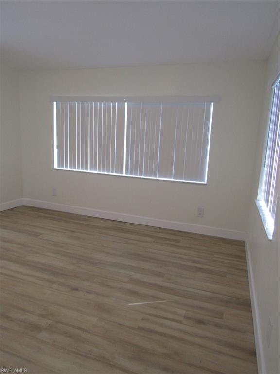 Spacious room featuring wood-finish flooring, white baseboards, and neutral wall tones