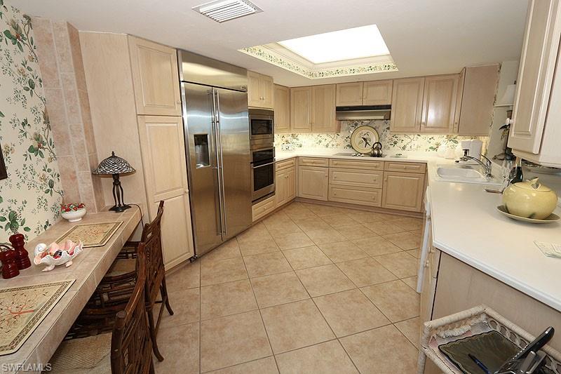 Kitchen featuring light-toned cabinetry, stainless steel side-by-side refrigerator, double wall ovens, and a countertop extension