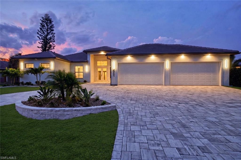 Mediterranean-style exterior featuring a paved driveway, two-car garage, manicured lawn, and a stone-clad planter with landscaping