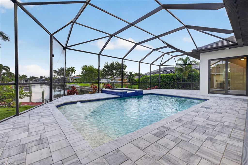 Screened outdoor living space featuring a rectangular pool with an integrated spa, a water feature, and grey paver decking