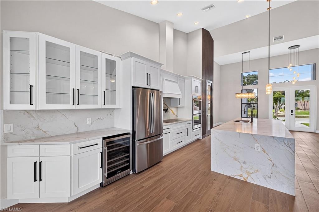 Gourmet kitchen featuring a waterfall island with stone countertop, stainless steel appliances, white cabinetry with black hardware, and wood-finish flooring