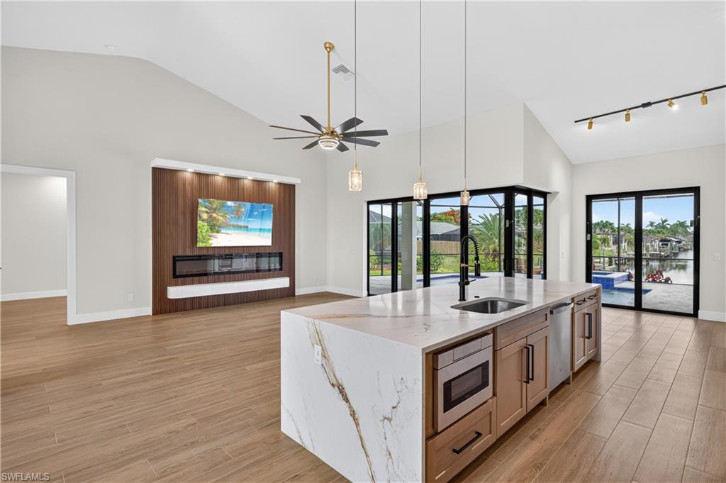 Open-concept living area featuring vaulted ceilings, wood-finish flooring, and a waterfall-edge island with integrated sink