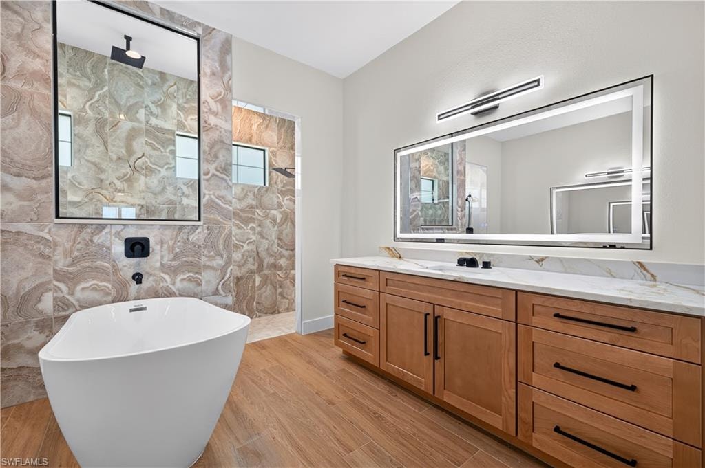 Modern bathroom featuring a freestanding soaking tub with matte black fixtures, an expansive vanity with wood-finish cabinetry and stone countertops, and a large illuminated mirror