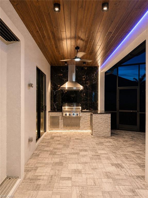 Outdoor kitchen featuring a built-in grill, stainless steel range hood, and a black marble-look backsplash