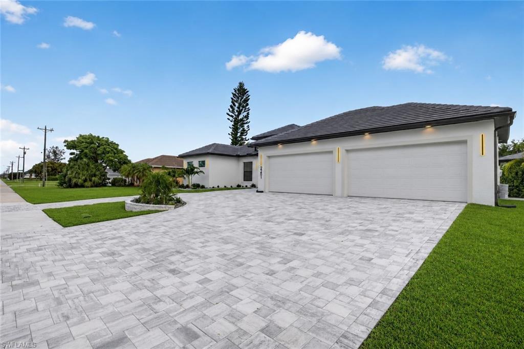 Modern exterior with a light stucco finish, featuring a paver driveway, dark tile roof, and integrated vertical lighting fixtures