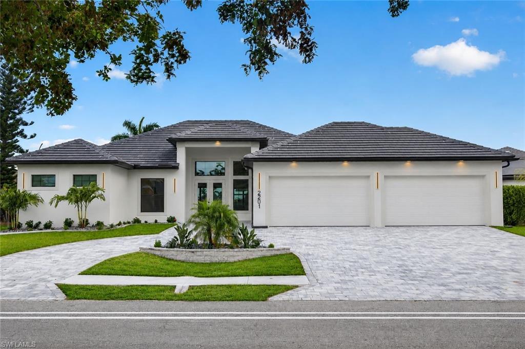 Contemporary stucco exterior featuring a two-car garage, tile roof, and paver driveway