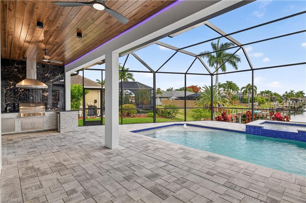 Screened outdoor living area featuring a custom pool, integrated spa, and a built-in outdoor kitchen