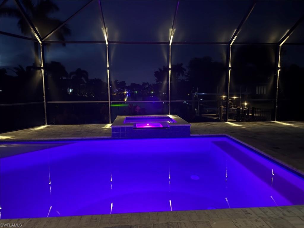 Screened pool enclosure featuring a pool with vibrant blue underwater lighting, an integrated hot tub with purple lighting, and patterned paver decking