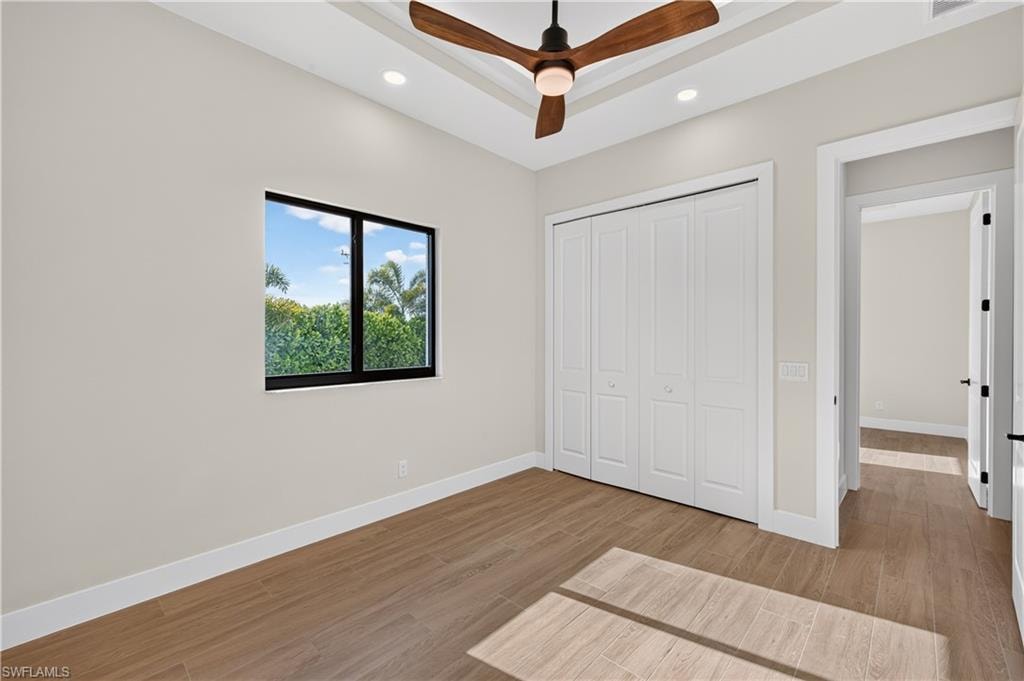 Tray ceiling featuring a modern ceiling fan, recessed lighting, and wood-finish flooring