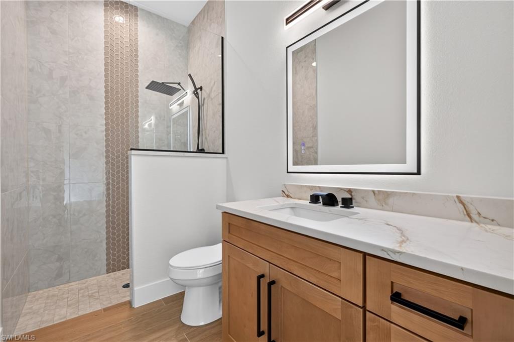 Modern bathroom featuring a light wood-finish vanity with black hardware, a rectangular undermount sink, and a stone-finish countertop