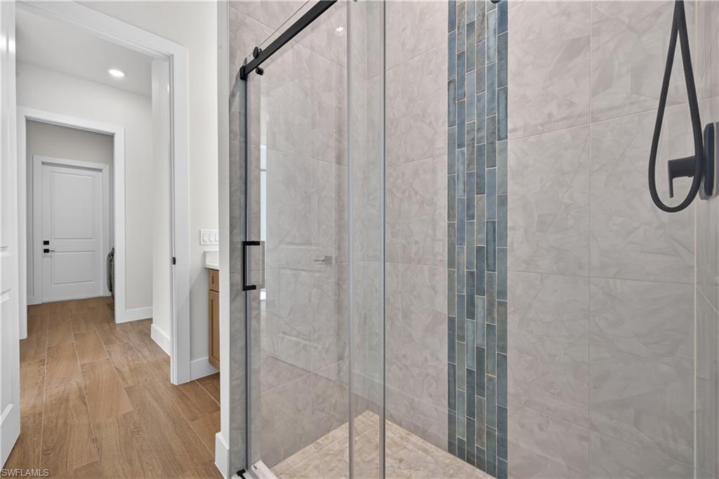 Modern shower enclosure featuring a sliding glass door with matte black hardware, large format tile surrounds, and a vertical mosaic accent stripe