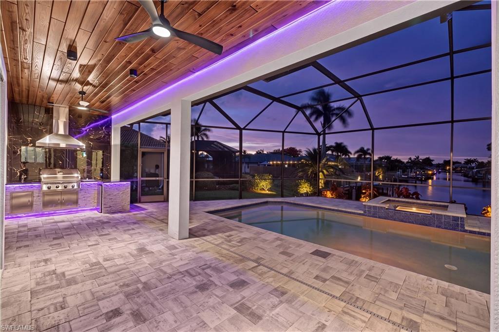 Screened outdoor living area featuring a built-in outdoor kitchen with stainless steel appliances, wood-finish plank ceiling, and recessed lighting