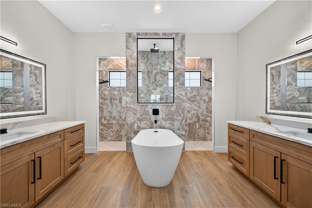 Contemporary bathroom featuring a freestanding soaking tub, wood-finish flooring, and dual vanity areas with white countertops