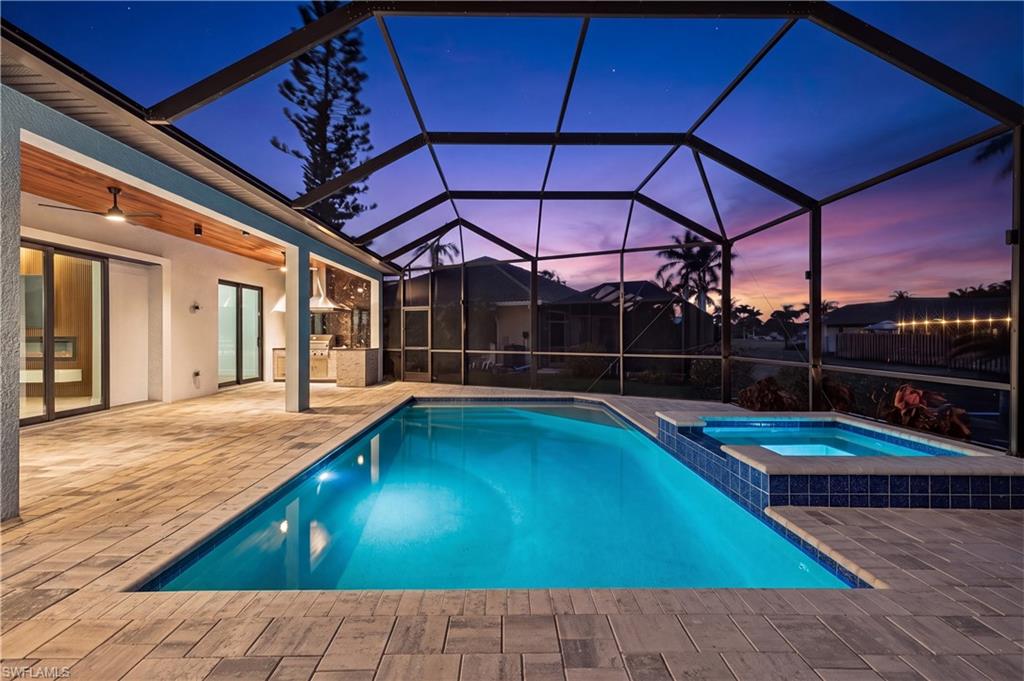 Screened enclosure featuring a swimming pool, integrated spa, and expansive paved patio