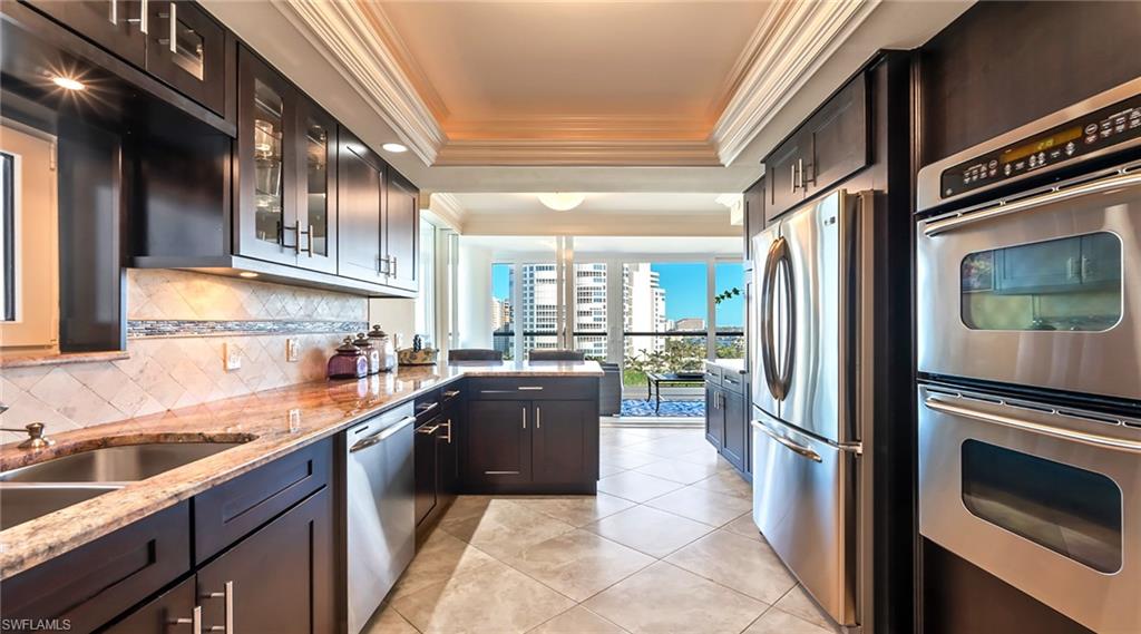 Kitchen with appliances with stainless steel finishes, ornamental molding, light stone counters, a tray ceiling, and glass insert cabinets