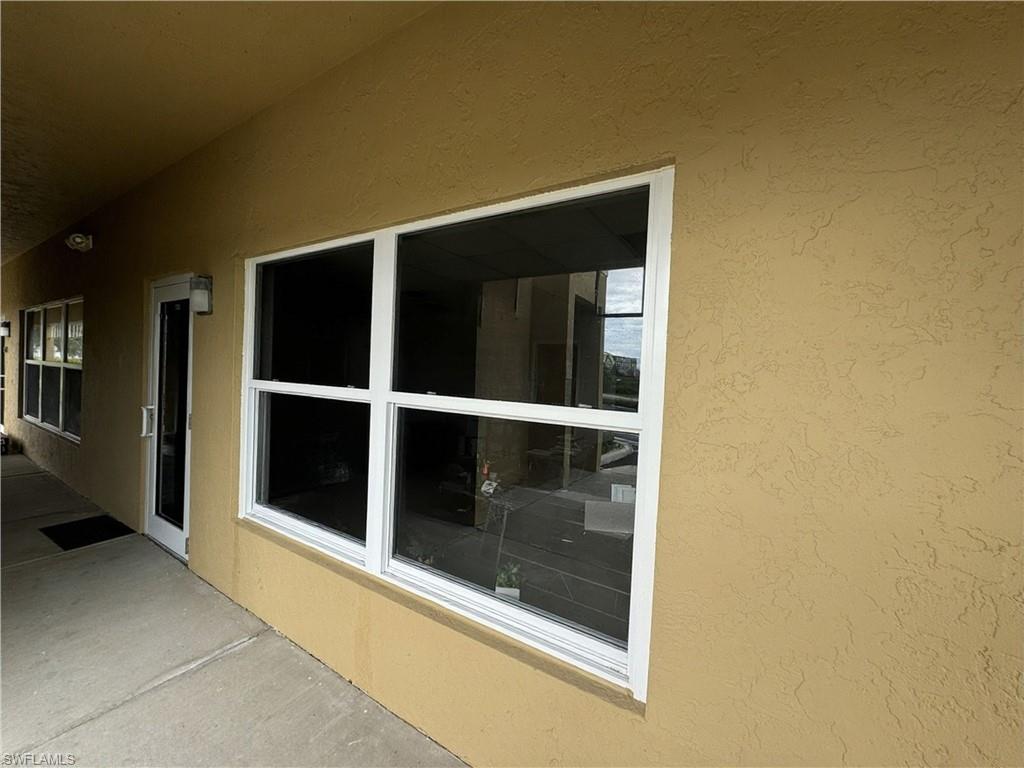Stucco exterior with multiple windows, concrete walkway, and an entry door with a sidelight
