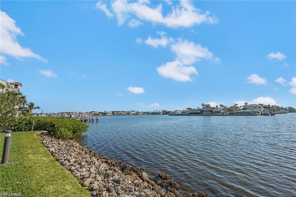 Waterfront property featuring a landscaped grassy area, rock shoreline, and surrounding water
