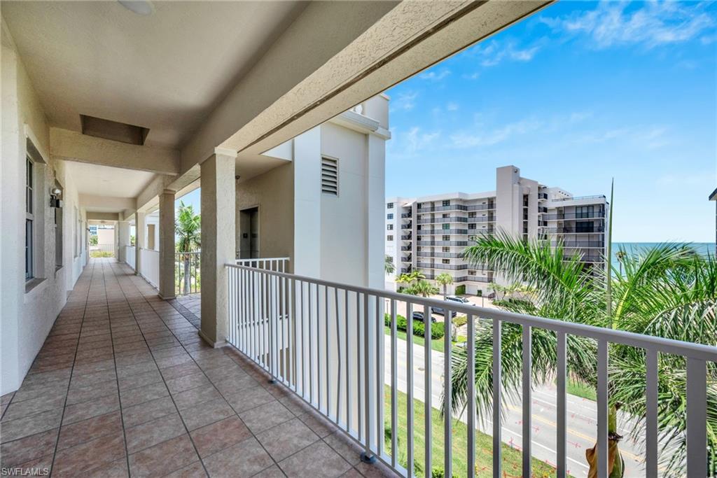 Outdoor walkway featuring tiled flooring and a white railing overlooking a street, palm trees, and the ocean