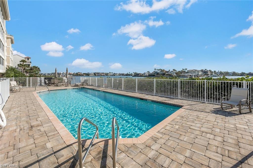 Swimming pool with paver decking, white perimeter fencing, and water frontage