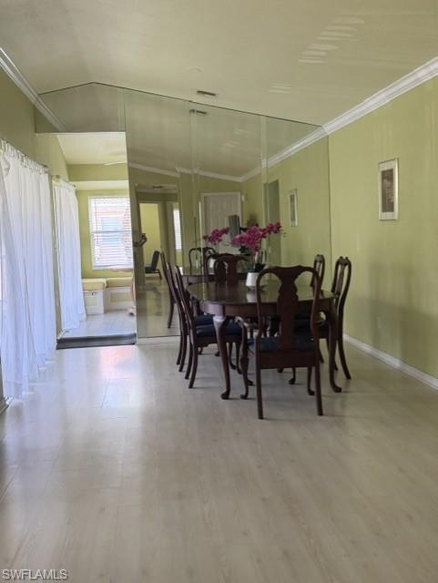 Spacious dining area featuring wood-finish flooring, a mirrored accent wall, and vaulted ceilings