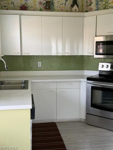 Corner kitchen with white cabinetry, light countertops, and a green subway tile backsplash