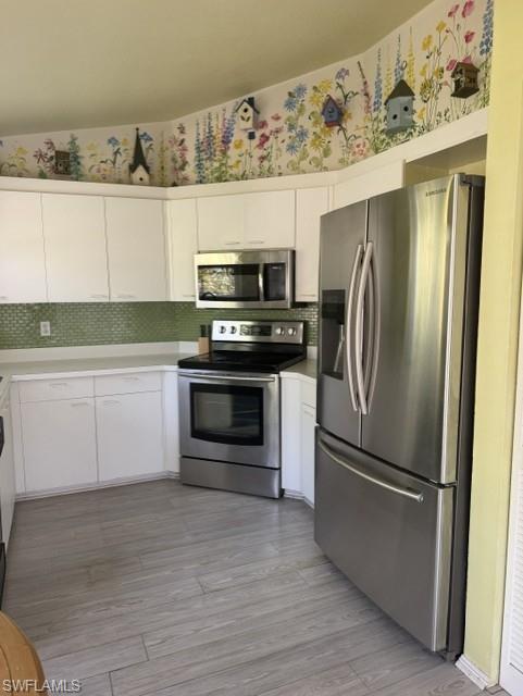Kitchen featuring stainless steel appliances, white cabinetry, green tile backsplash, light wood-finish flooring, and white countertops