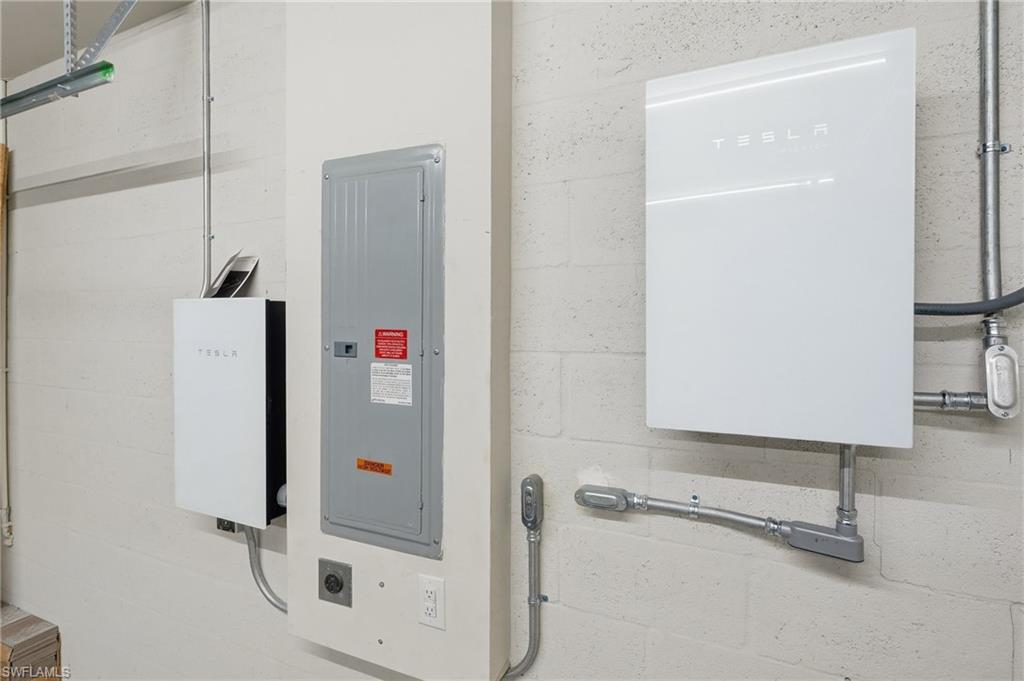 Two Tesla Powerwall units with an electrical panel and conduit systems on a concrete block wall