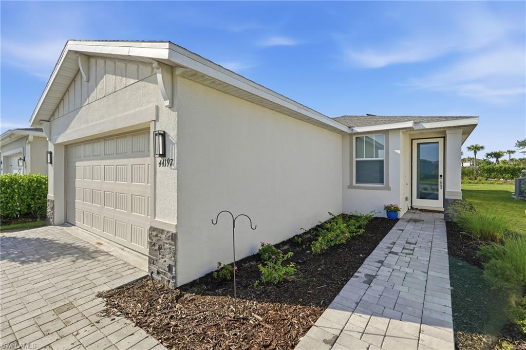 Contemporary stucco exterior with a paneled garage door, stone accent details, paver driveway, paver walkway, and a full-light entry door