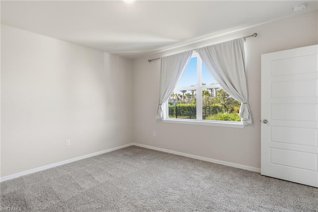 Bright interior room featuring a large window with exterior greenery, neutral wall color, and plush gray carpeting