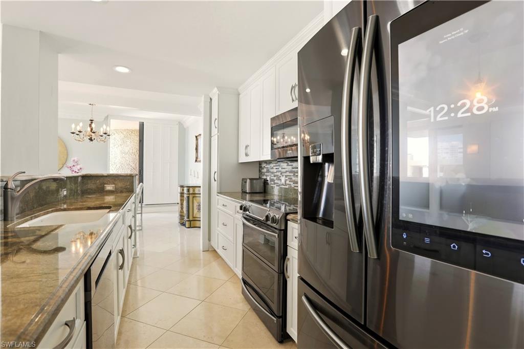 Kitchen featuring stainless steel appliances, dark stone counters, white cabinetry, light tile patterned floors, and hanging lights