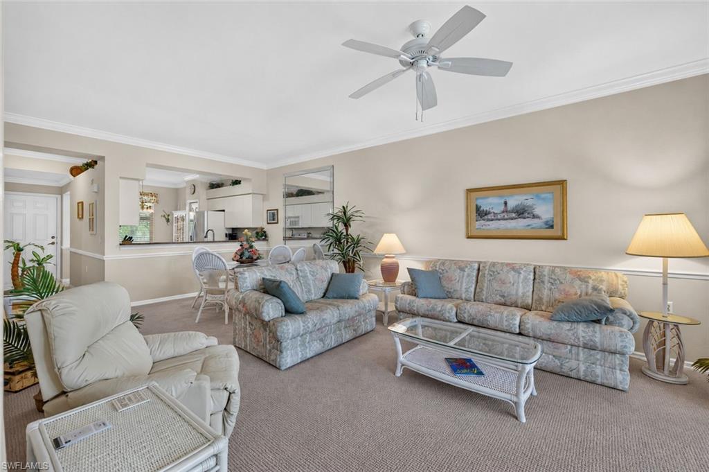 Carpeted living area featuring crown molding, a ceiling fan with light fixture, and neutral wall paint