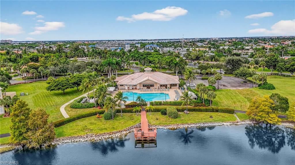 Expansive waterfront property featuring a large community building with a swimming pool, a wooden pier, and a surrounding landscape of mature trees and manicured lawns