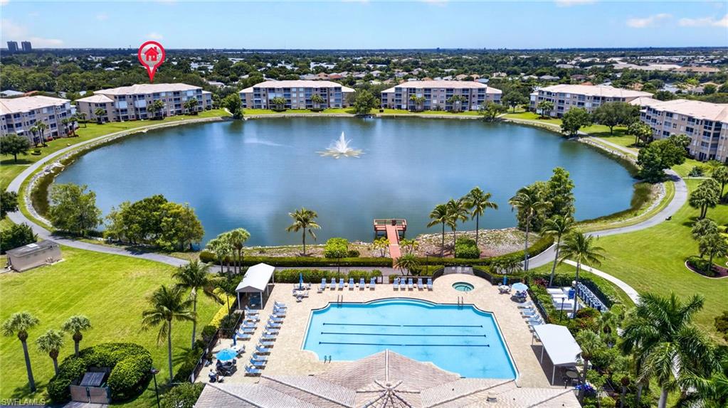 Expansive community grounds featuring a large central lake with a fountain, multiple residential buildings, an outdoor swimming pool with lane markers, a separate spa, and manicured green spaces