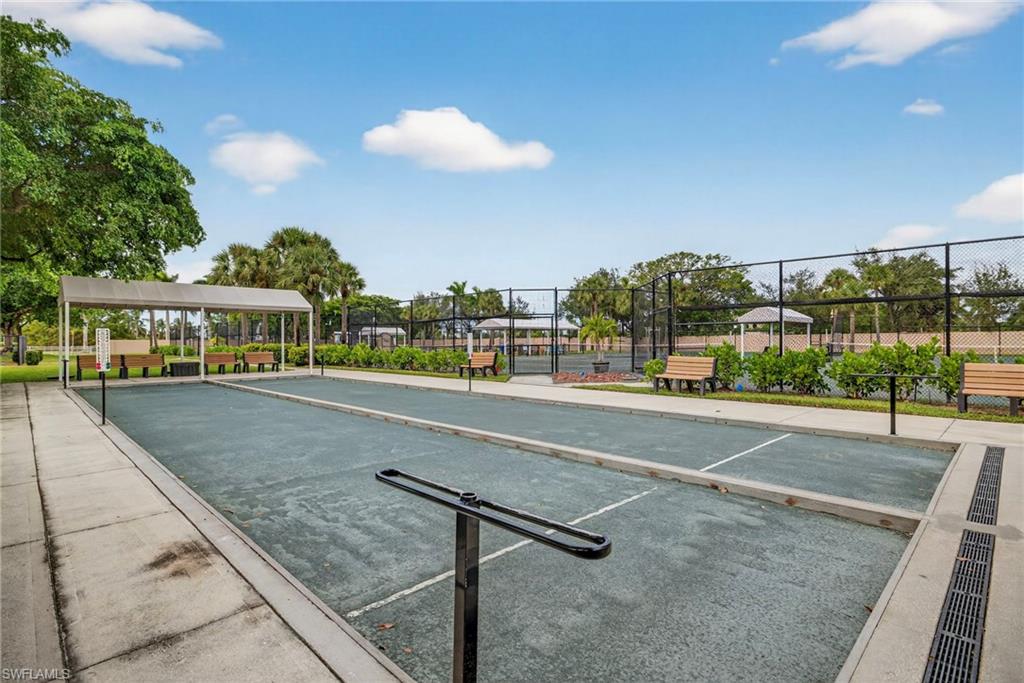 Dual bocce courts featuring perimeter concrete pathways, a covered seating area with multiple benches, and surrounding mature landscaping