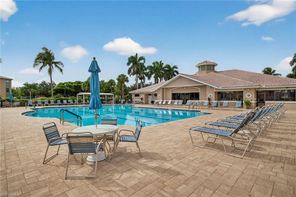Community pool area featuring a large swimming pool, extensive paver deck, and a clubhouse with a tiled roof