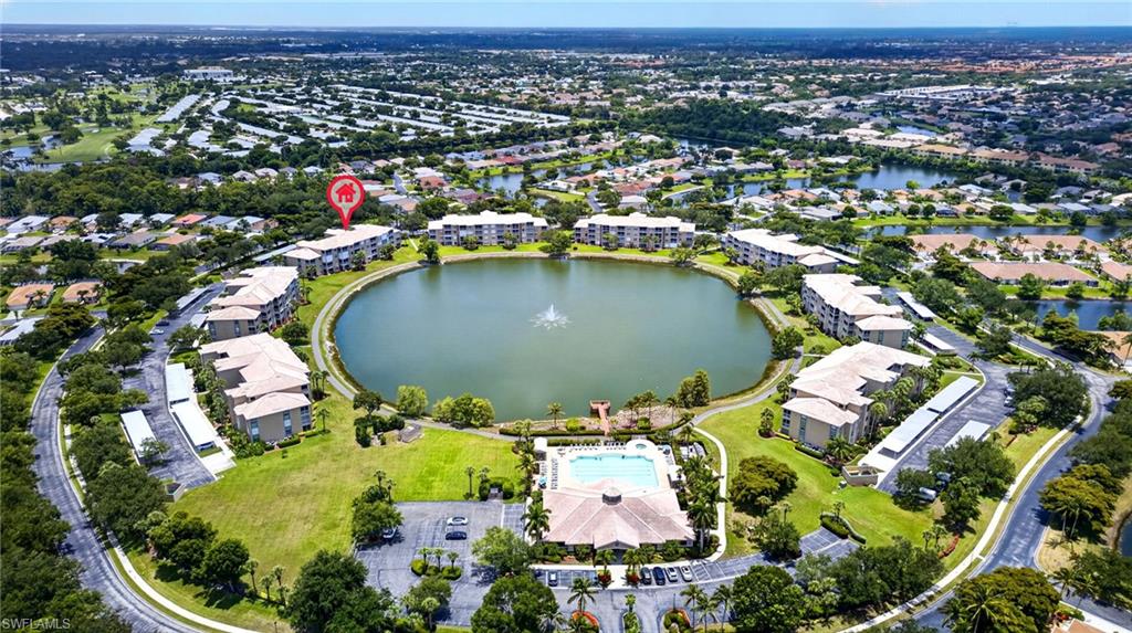 Aerial overview of a community featuring apartment buildings encircling a central lake with a fountain