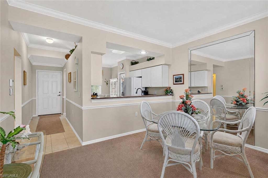 Dining area featuring a built-in wall mirror, crown molding, and neutral-toned carpet flooring