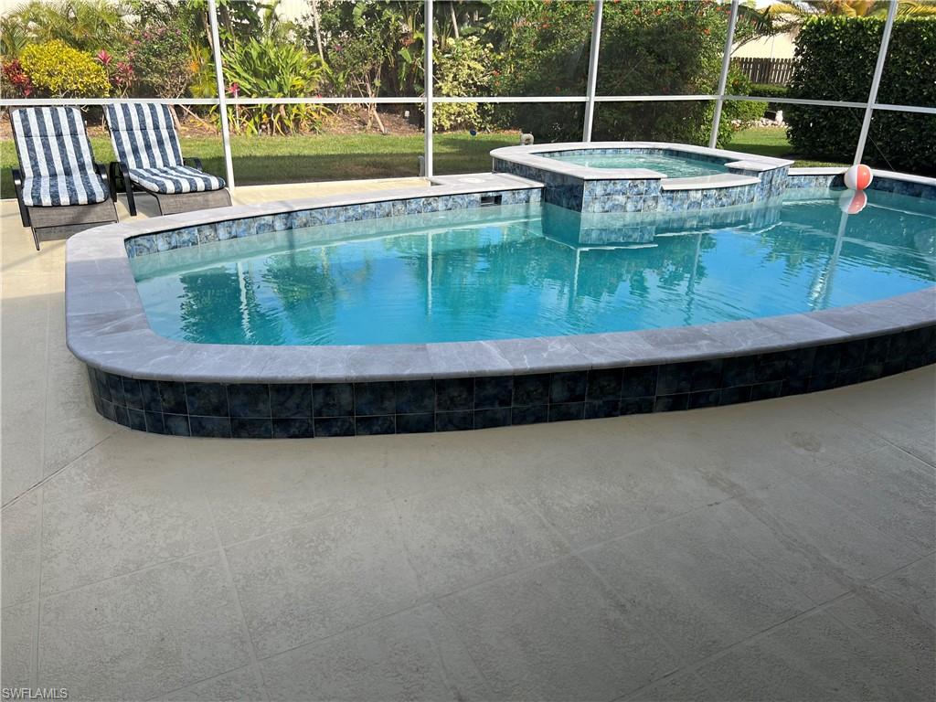 View of swimming pool featuring an in ground hot tub, glass enclosure, and a patio area