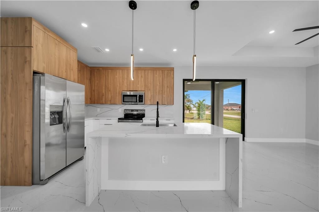 Modern kitchen featuring a waterfall island with white marble-look countertop, wood-finish cabinetry, stainless steel appliances, and sleek pendant lighting
