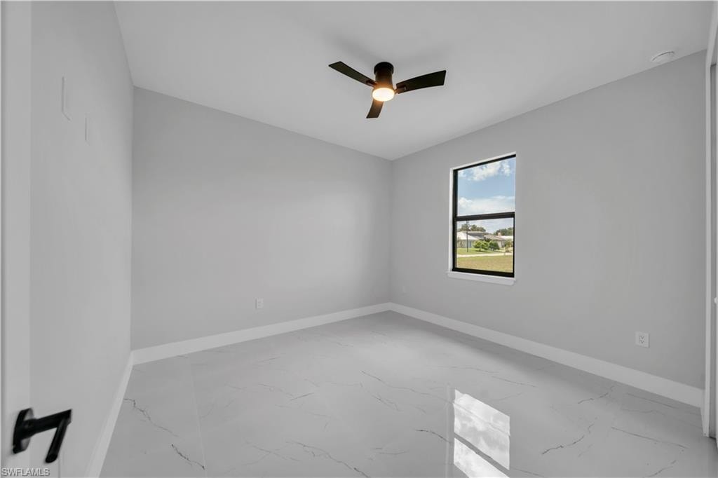 Spacious room featuring large format tile flooring, a window with black trim, a ceiling fan with integrated lighting, clean white baseboards, and neutral wall paint