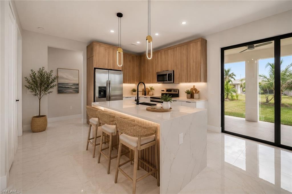 Gourmet kitchen featuring a large waterfall island with integrated lighting, wood-finish cabinetry, stainless steel appliances, and sleek pendant lighting
