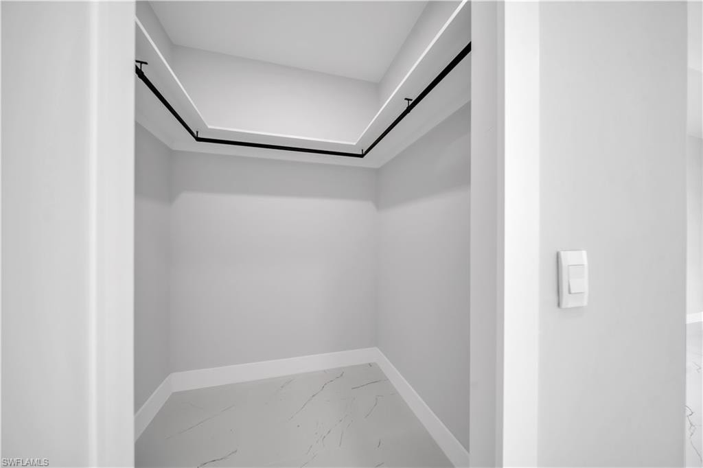 Walk-in closet with perimeter hanging rods, recessed ceiling lighting, light gray walls, and white marble-patterned flooring