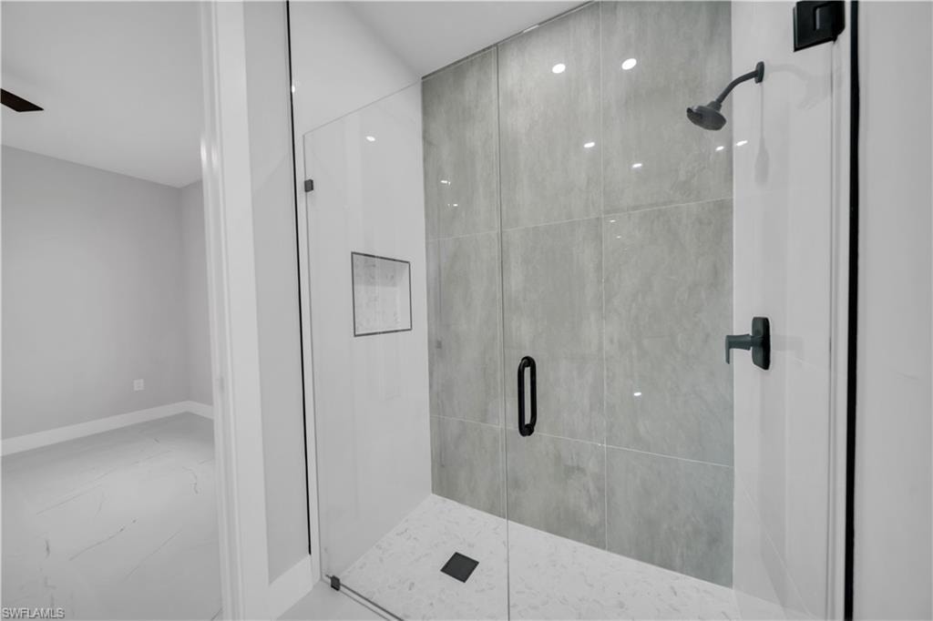 Frameless glass shower enclosure featuring large format grey wall tiling, a built-in shower niche, and matte black fixtures